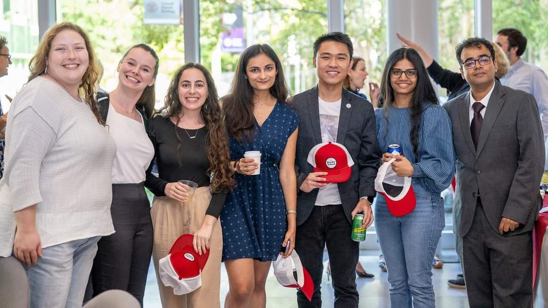 MPA students pose for a group photo at the Brooks Anniversary Party and hold Brooks trucker hats