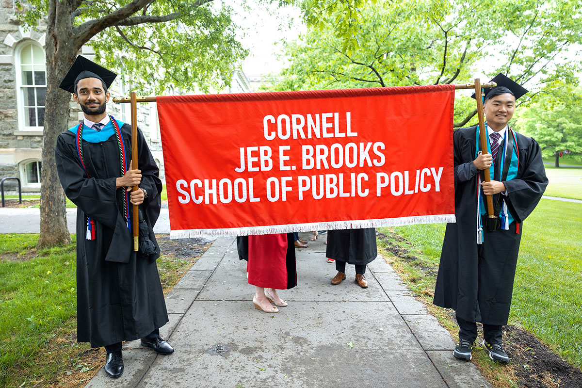 Two Brooks students, in academic graduation gowns, holding Brooks School graduation banner