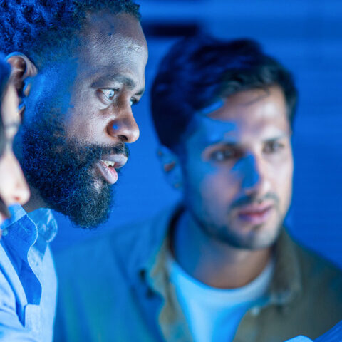 Three people looking at computer screen with blue glowing background