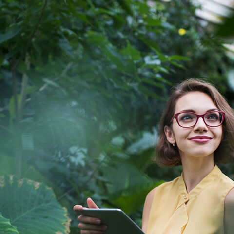Woman with clipboard standing in botanical garden surrounded by plants
