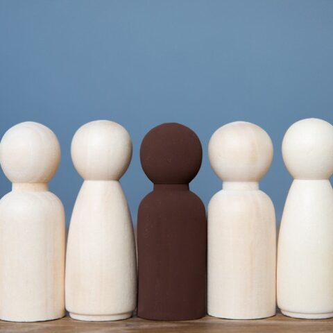 Row of wooden figures, five white, one brown.