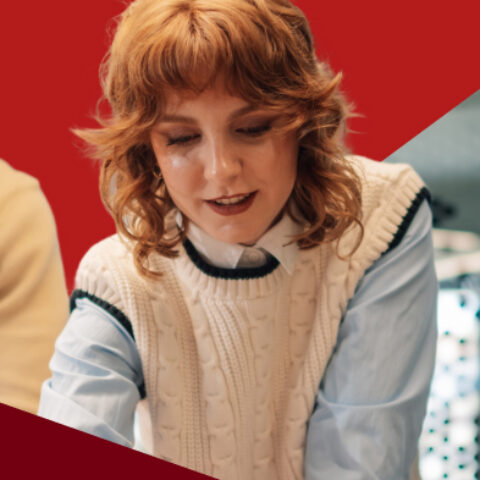 Woman with red hair working in a group, looking down at a project, red triangle overlay