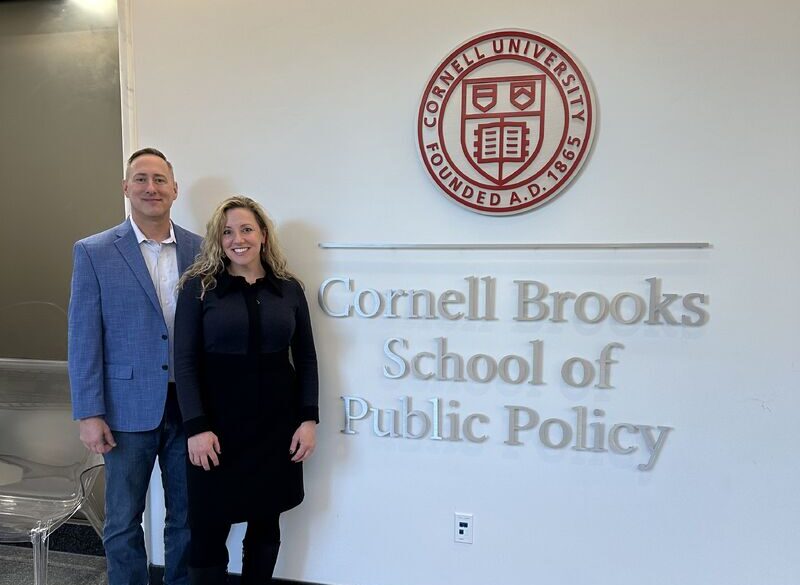Two people standing next to the Cornell Brooks School of Public Policy sign