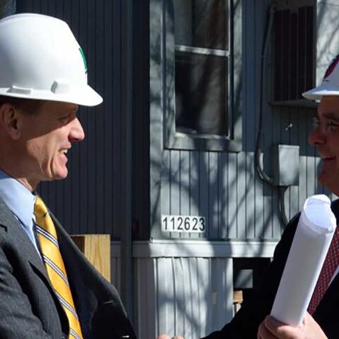 Two men wearing hardhats talking in front of a building
