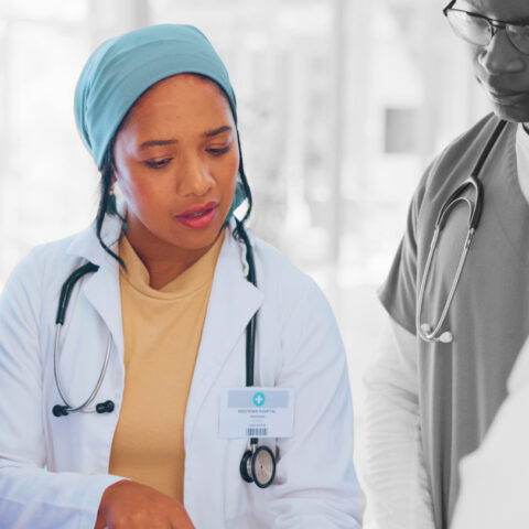 Women in the medical field wearing a stethoscope pointing and discussing a document with a coworker