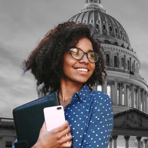 Woman in blue and white polka-dot shirt holding a computer and cell phone, black and white background of the Capitol Building