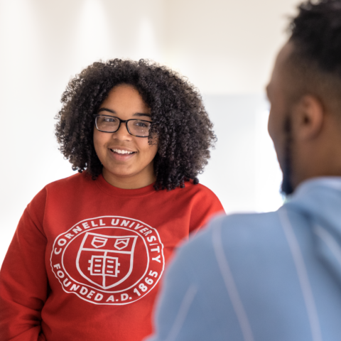 Smiling student wearing a red sweatshirt sitting across from a male student