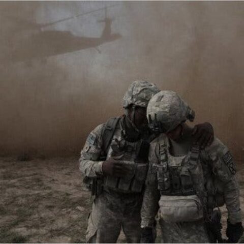 two soldiers standing in dust spinning from helicopter in the background