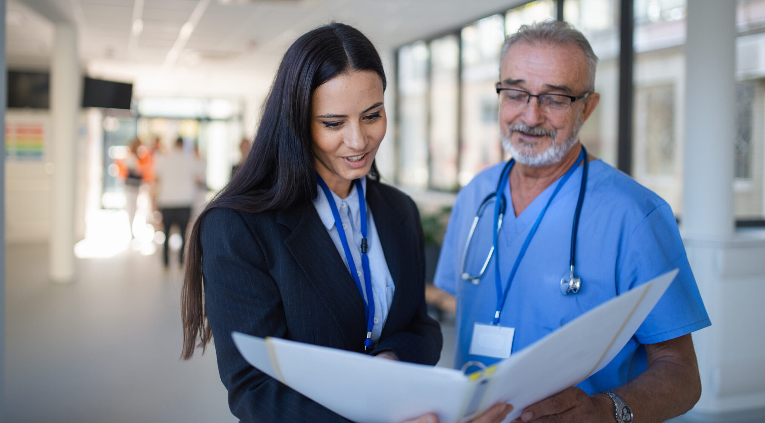 Two healthcare professionals reviewing a document in a hospital corridor.