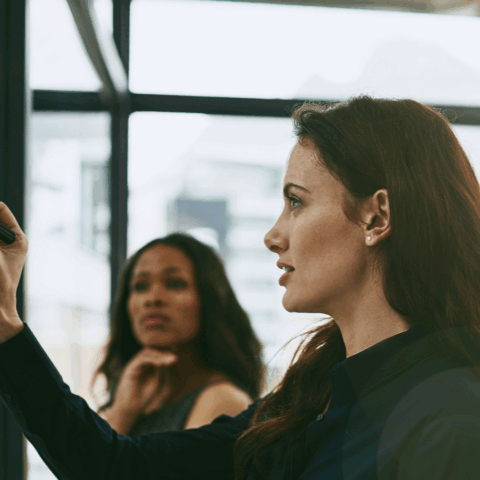 young female professional strategizing with others at a marked up whiteboard
