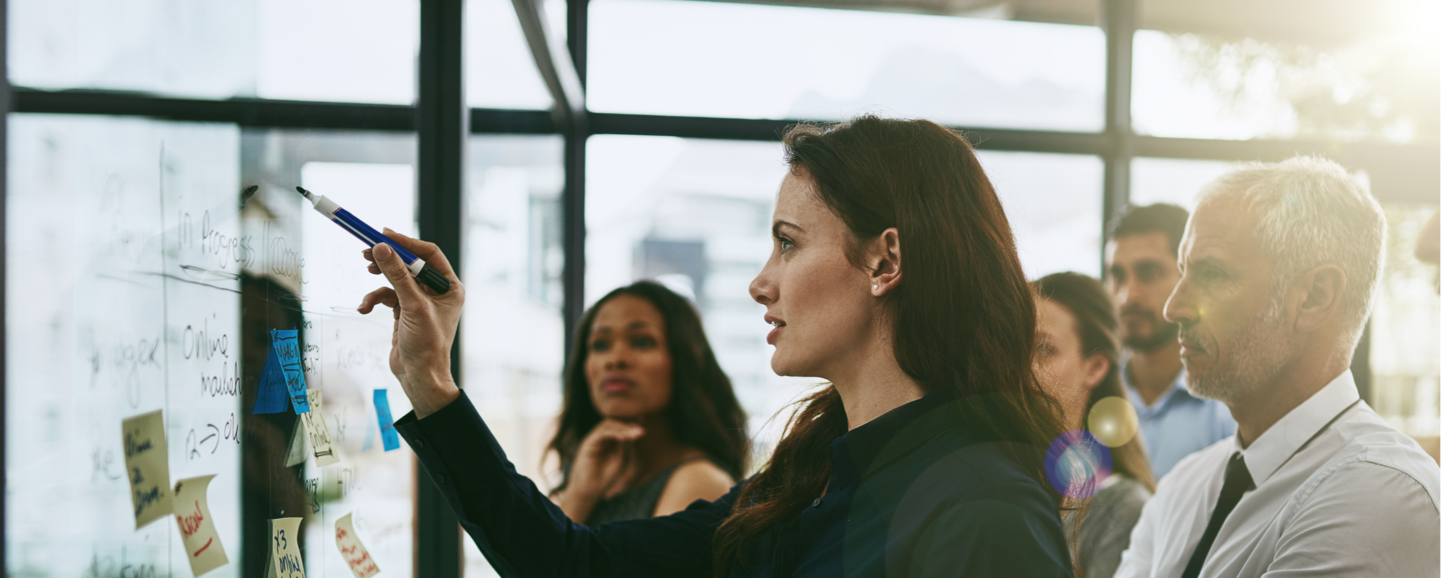 young female professional strategizing with others at a marked up whiteboard
